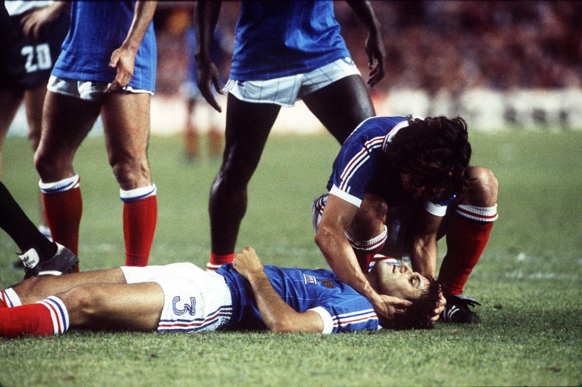 Jeden ze spoluhráčů se sklání ke zraněnému francouzskému obránci Patricku Battistonovi, který upadl do bezvědomí po střetu s německým brankářem Haraldem Schumacherem v semifinále mistrovství světa 1982 ve španělské Seville. 