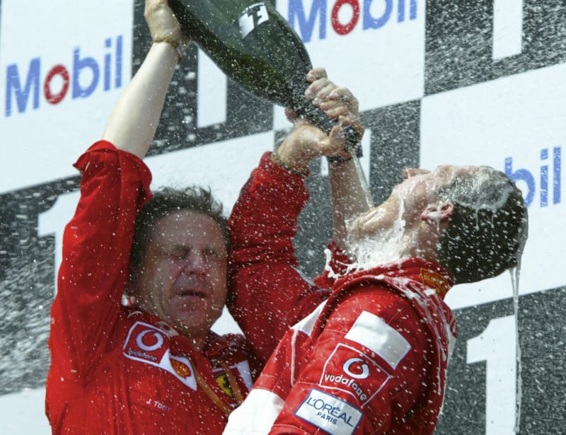 Německý pilot formule 1 Michael Schumacher (vlevo) pije za pomoci ředitele stáje Ferrari Jean Todt šampaňské po vítězství a zisku titulu mistra světa 2002 ve francouzském Magny Cours.
