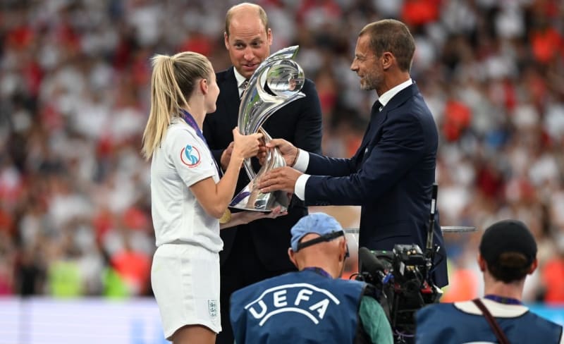 Princ William (uprostřed) hledí na kapitánku anglické reprezentace Leah Williamsonovou, jak přebírá trofej pro fotbalové mistryně Evropy z rukou prezidenta Evropské fotbalové unie Aleksandera Čeferina. 