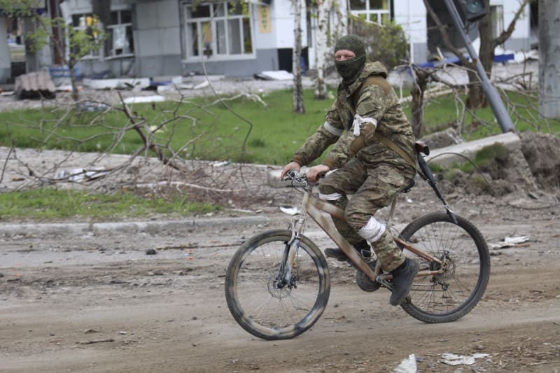 Proruský separatista z Doněcké lidové republiky jede na kole zničenými ulicemi Mariupolu.