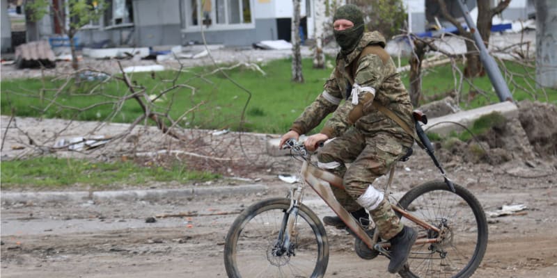 Proruský separatista z Doněcké lidové republiky jede na kole zničenými ulicemi Mariupolu. (4. květen 2022)