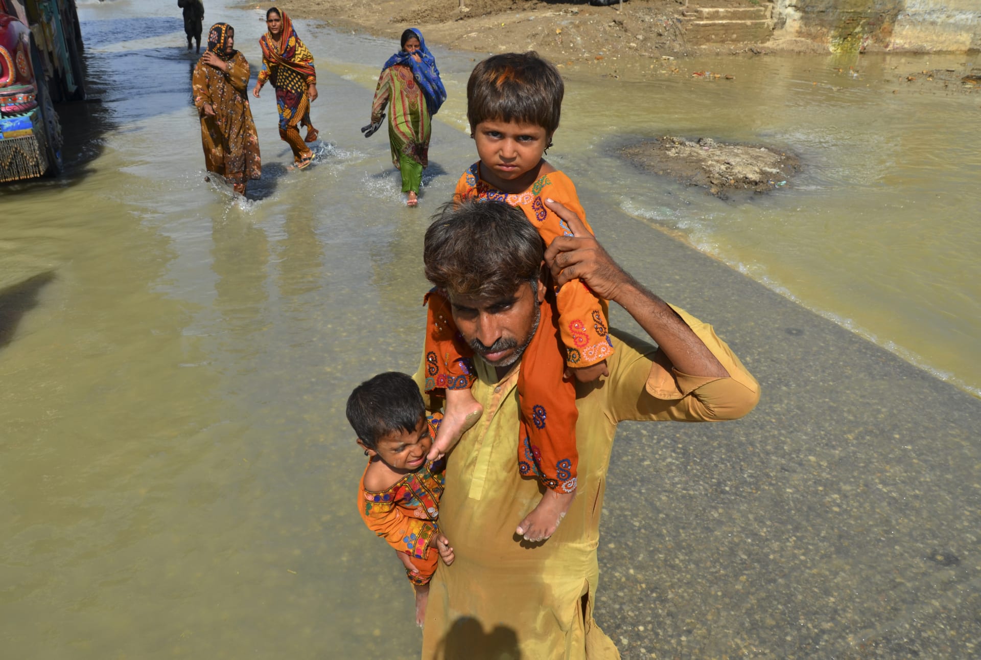 Muž nese své dcery z domu postiženého povodněmi, brodí se zaplavenou oblastí v Džafarabádu. (27. 8. 2022)