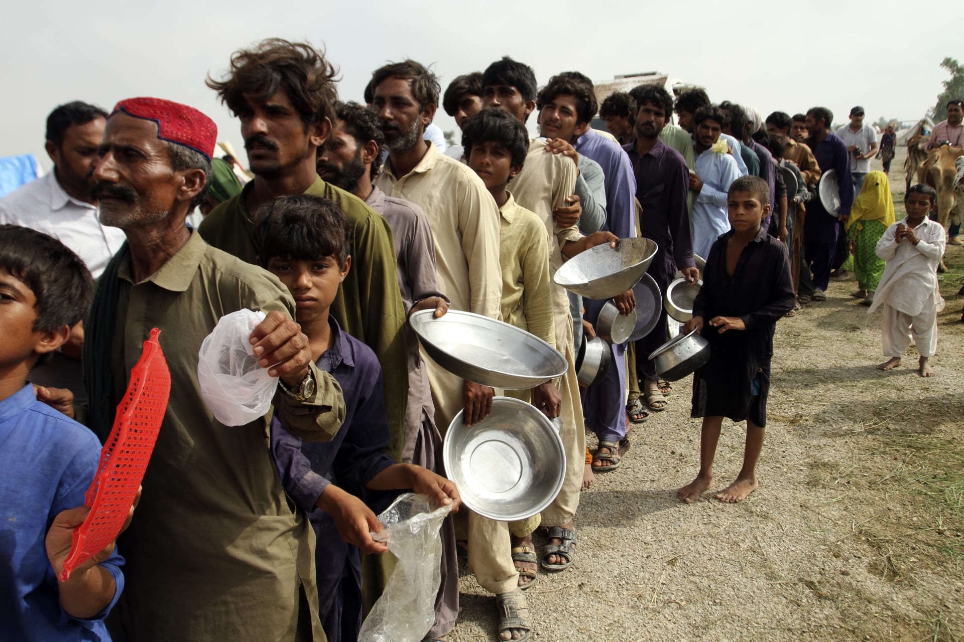 Lidé stojí v dlouhé frontě s nádobím na jídlo, které rozdávají jednotky pákistánské armády. (27. 8. 2022)