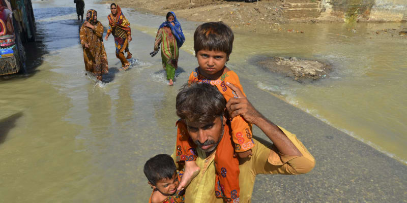 Muž nese své dcery z domu postiženého povodněmi, brodí se zaplavenou oblastí v Džafarabádu. (27. 8. 2022)