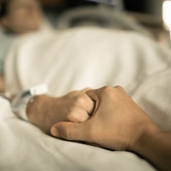Muž drží ženu za ruku na nemocničním lůžku
