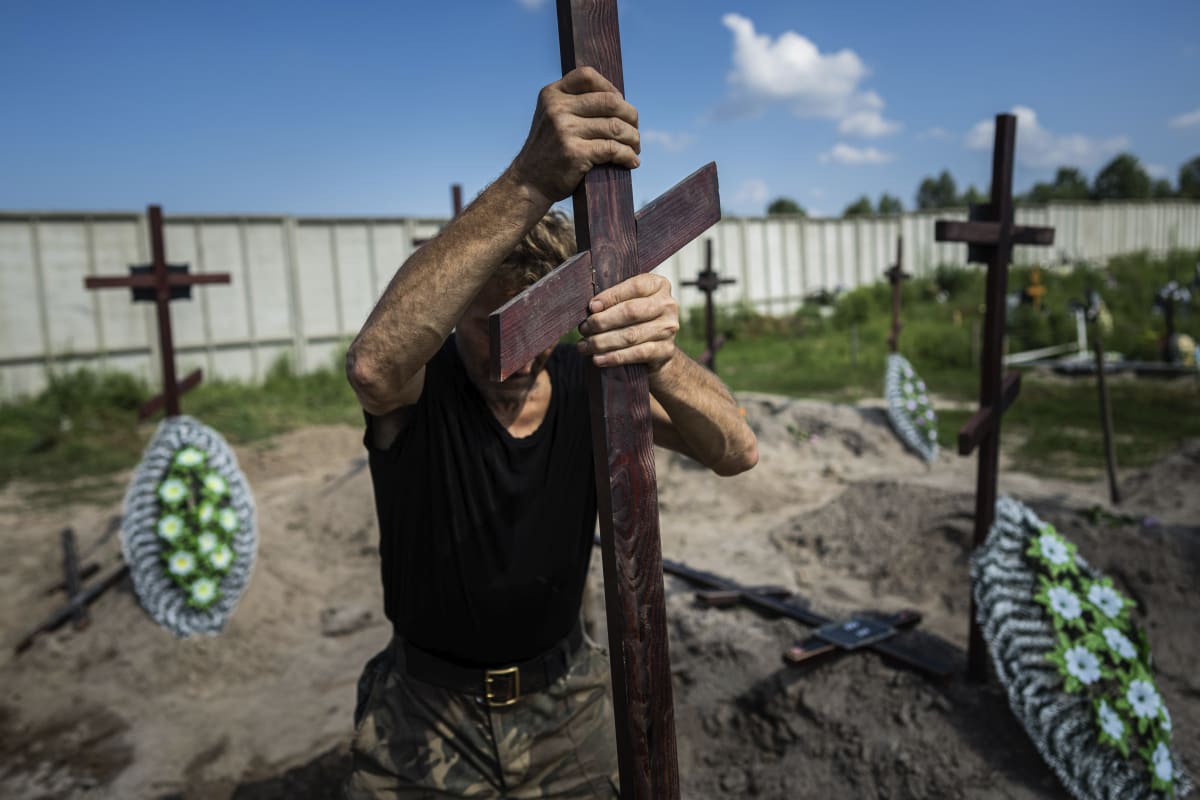 Zaměstnanec hřbitova instaluje kříž na hrob civilisty, jehož tělo bylo nalezeno v jednom z masových hrobů v Buči