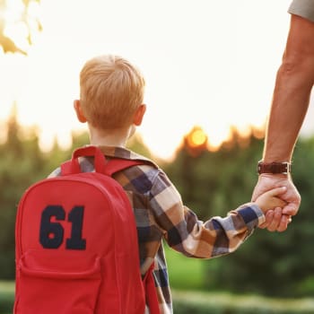 Chlapec s batohem a otcem na cestě do školy