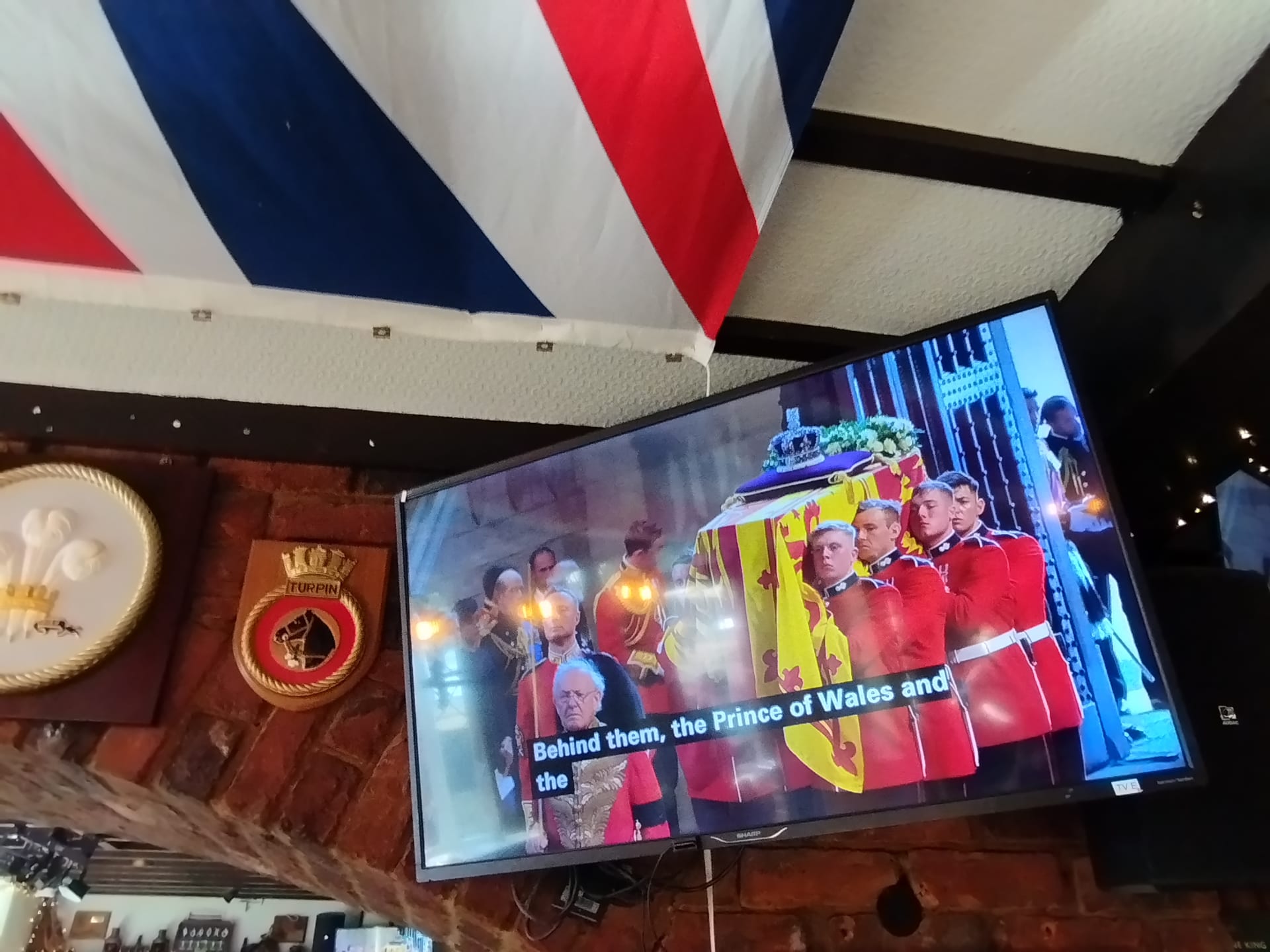 Na pintě piva s královnou. Výčep The Ship Anson v Portsmouthu. Televizory tady přenášejí celý den přímý přenos ze smutečních obřadů a loučení s královnou ve Westminsterském paláci v Londýně.
