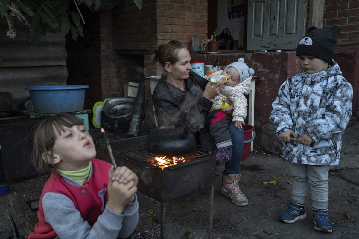 Matka se svými třemi dětmi před domem ve válkou zničeném Izjumu