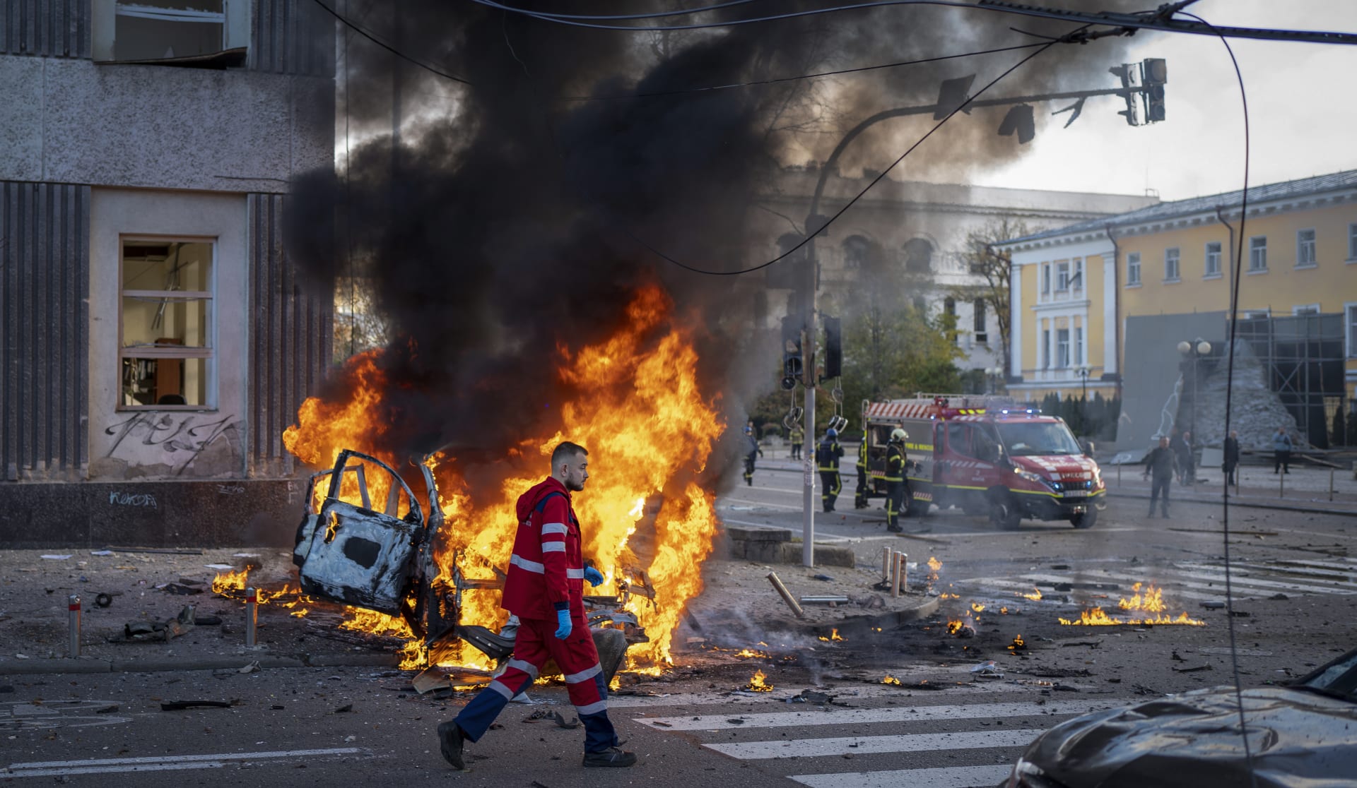 Ukrajinský záchranář jde kolem hořícího auta po ruském bombardování.
