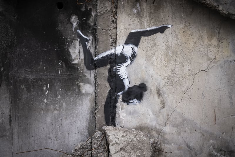 Na zdi zničené budovy ve městě Irpiň 11. listopadu 2022 v Kyjevské oblasti na Ukrajině je vidět graffiti ženy v trikotu a s nákrčníkem mávající stuhou. Tento snímek ale Banksy zatím na svém Instagramu nezveřejnil. 