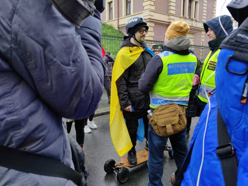 Před protivládním průvodem se objevil muž na elektrickém skateboardu a s ukrajinskou vlajkou na zádech.