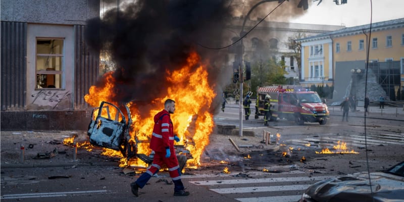 Ukrajinský záchranář jde kolem hořícího auta po ruském bombardování Kyjeva. (11. října 2022)