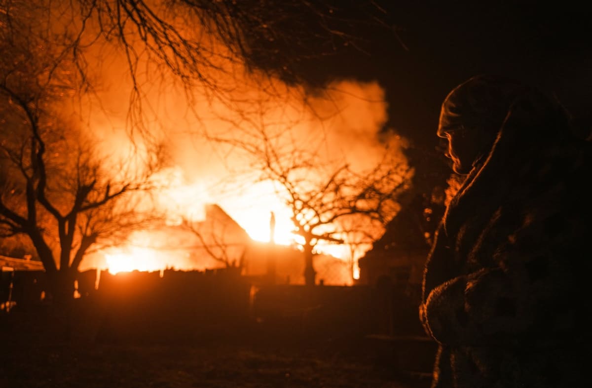 Žena sleduje požár domu po ruském ostřelování obce Ivanivka nedaleko Bachmutu