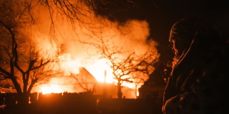 Žena sleduje požár domu po ruském ostřelování obce Ivanivka nedaleko Bachmutu