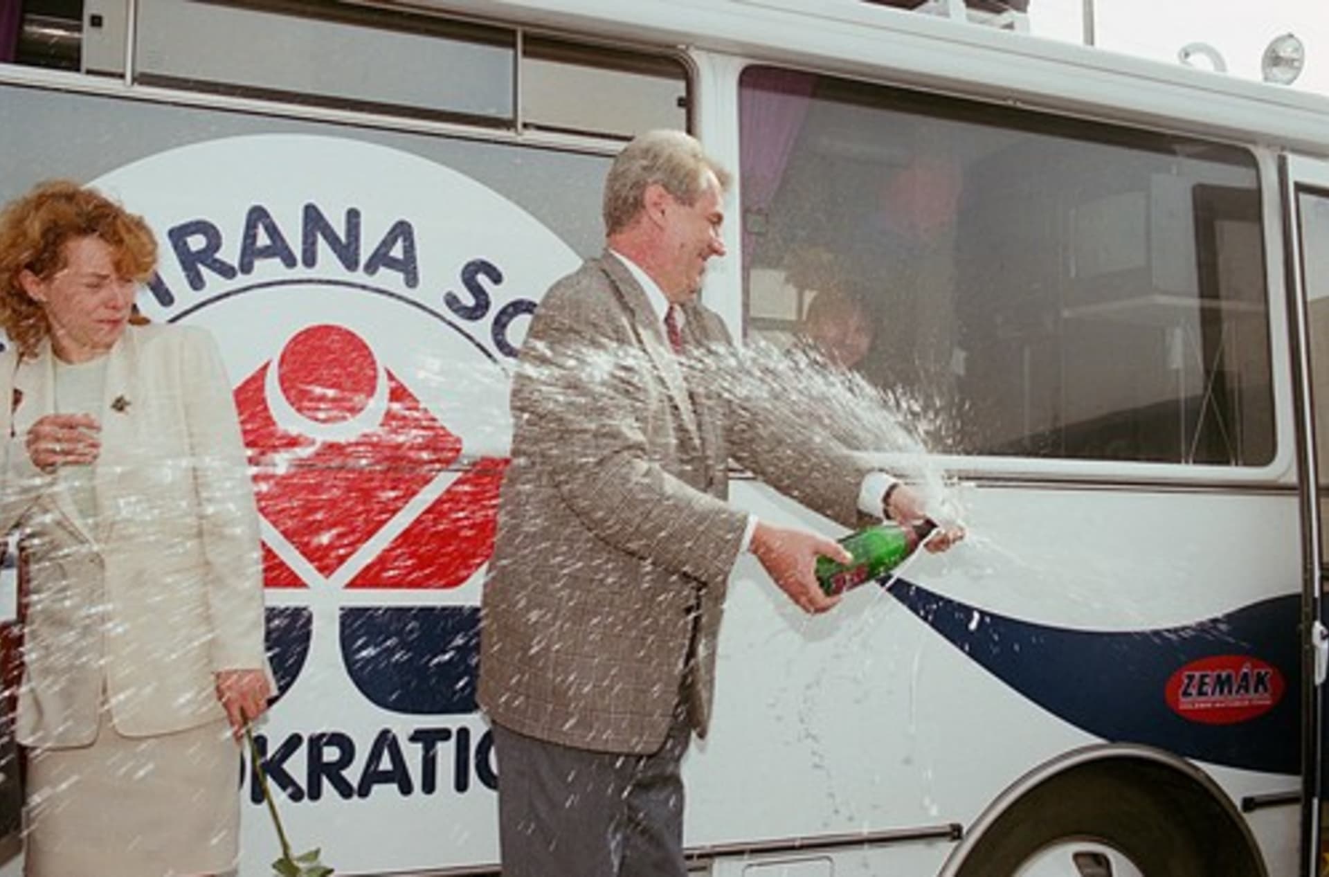 Miloš Zeman právě křtí svůj volební autobus Zemák, salvě šampaňského uhýbá Petra Buzková. 
