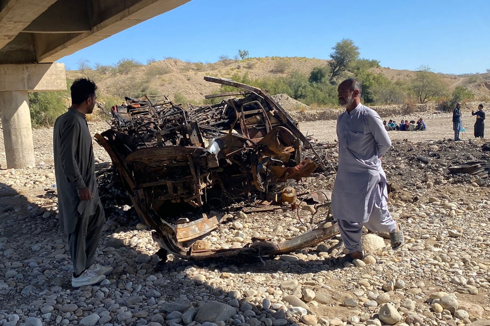 Obyvatelé se dívají na vrak shořelého osobního autobusu v okrese Lasbela v pákistánské provincii Balúčistán 29. ledna 2023. 