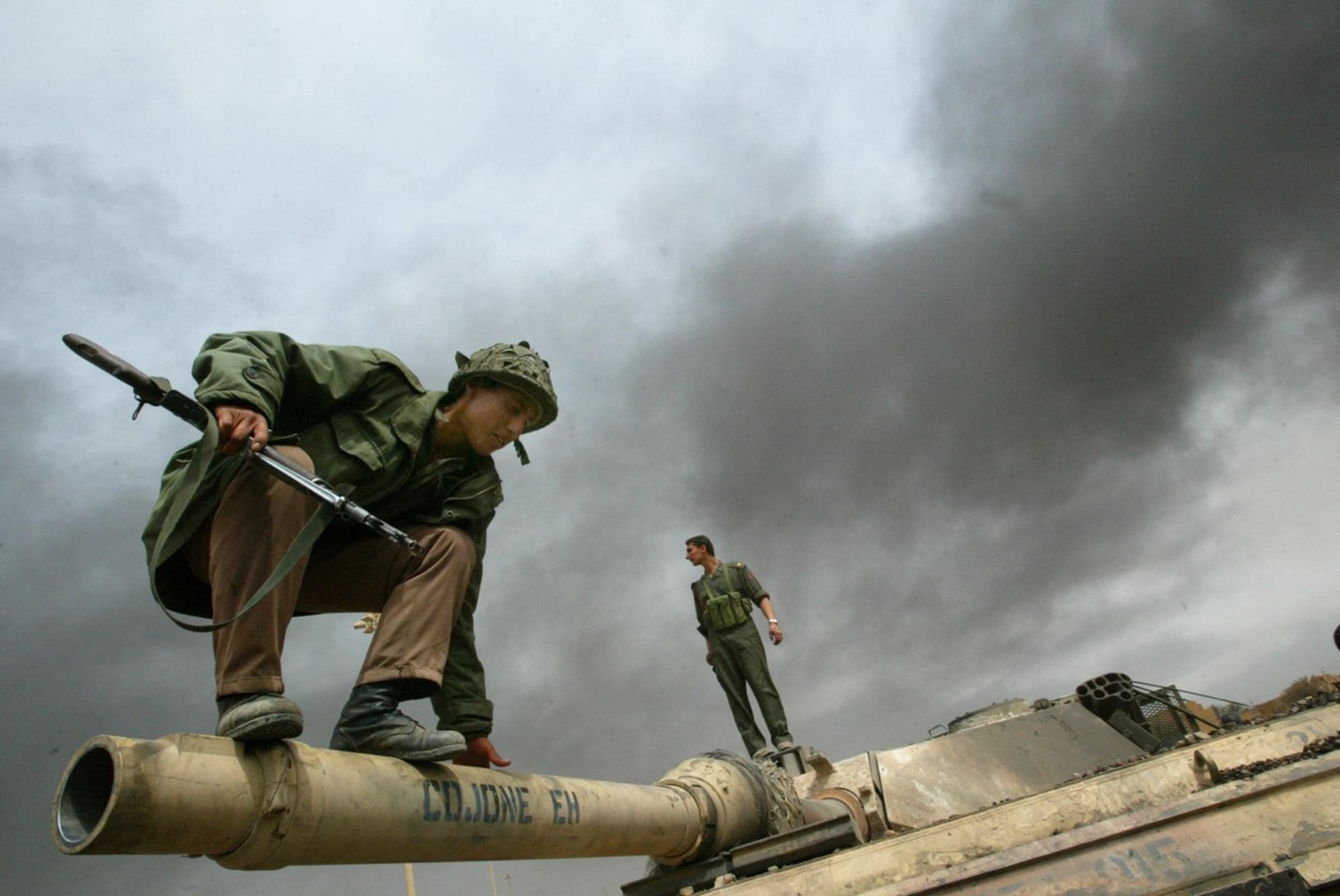 Příslušník irácké milice skáče z hlavně tanku M1A2 Abrams zničeného během těžkých bojů na okraji Bagdádu v roce 2003