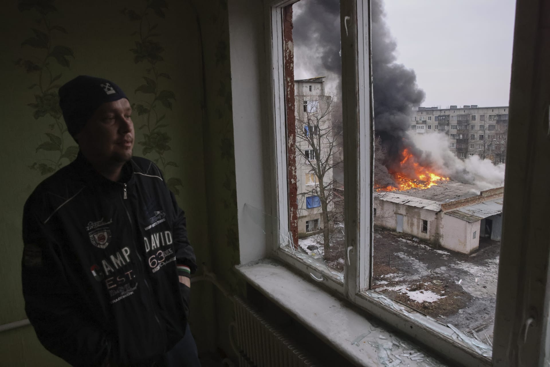Muž z okna sleduje následky ruského ostřelování města Časiv Jar v Doněcké oblasti.