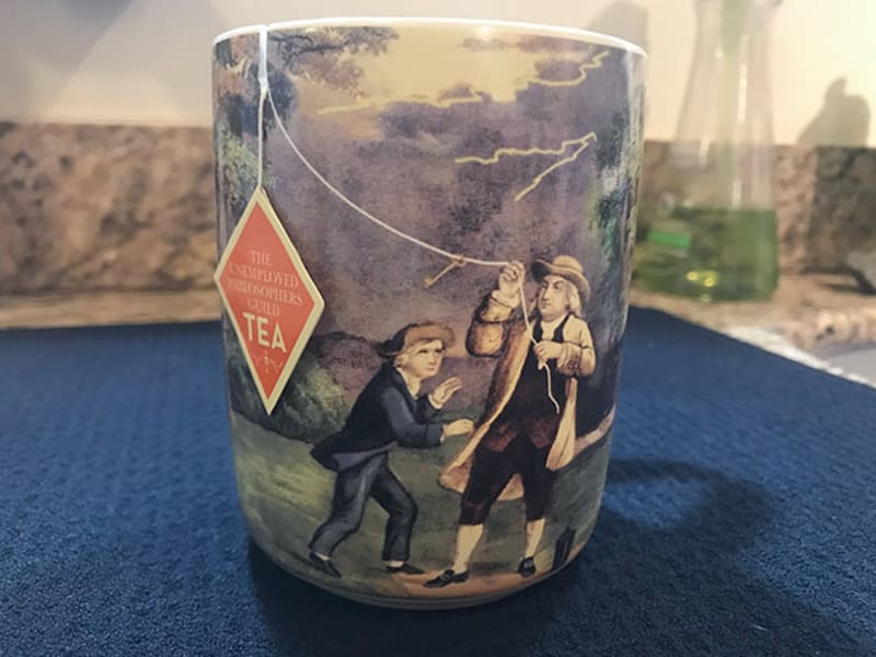 Hrnek s Benjaminem Franklinem, který cedulku na konci čaje drží jako papírového draka