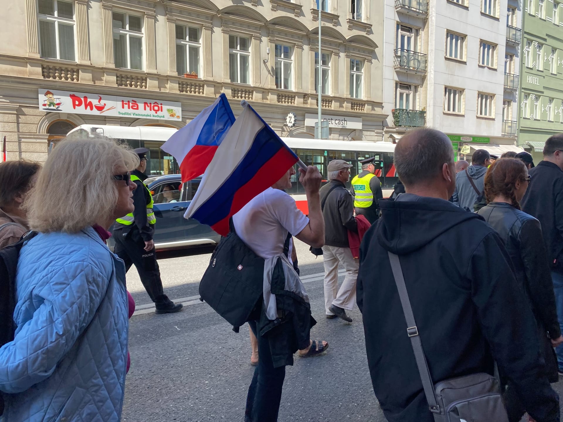 Na mírovém pochodu vlaje i ruská vlajka. Na demonstraci dohlížejí těžkooděnci.