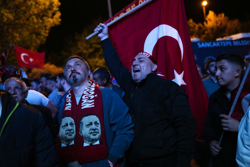 Příznivci tureckého prezidenta Recepa Tayyipa Erdogana sledují zprávy na obří obrazovce před sídlem Strany spravedlnosti a rozvoje (AKP) v tureckém Istanbulu v neděli 14. května 2023. Hlasovat mohlo více než 64 milionů lidí, včetně 3,4 milionu voličů ze zahraničí. (AP Photo/Francisco Seco)