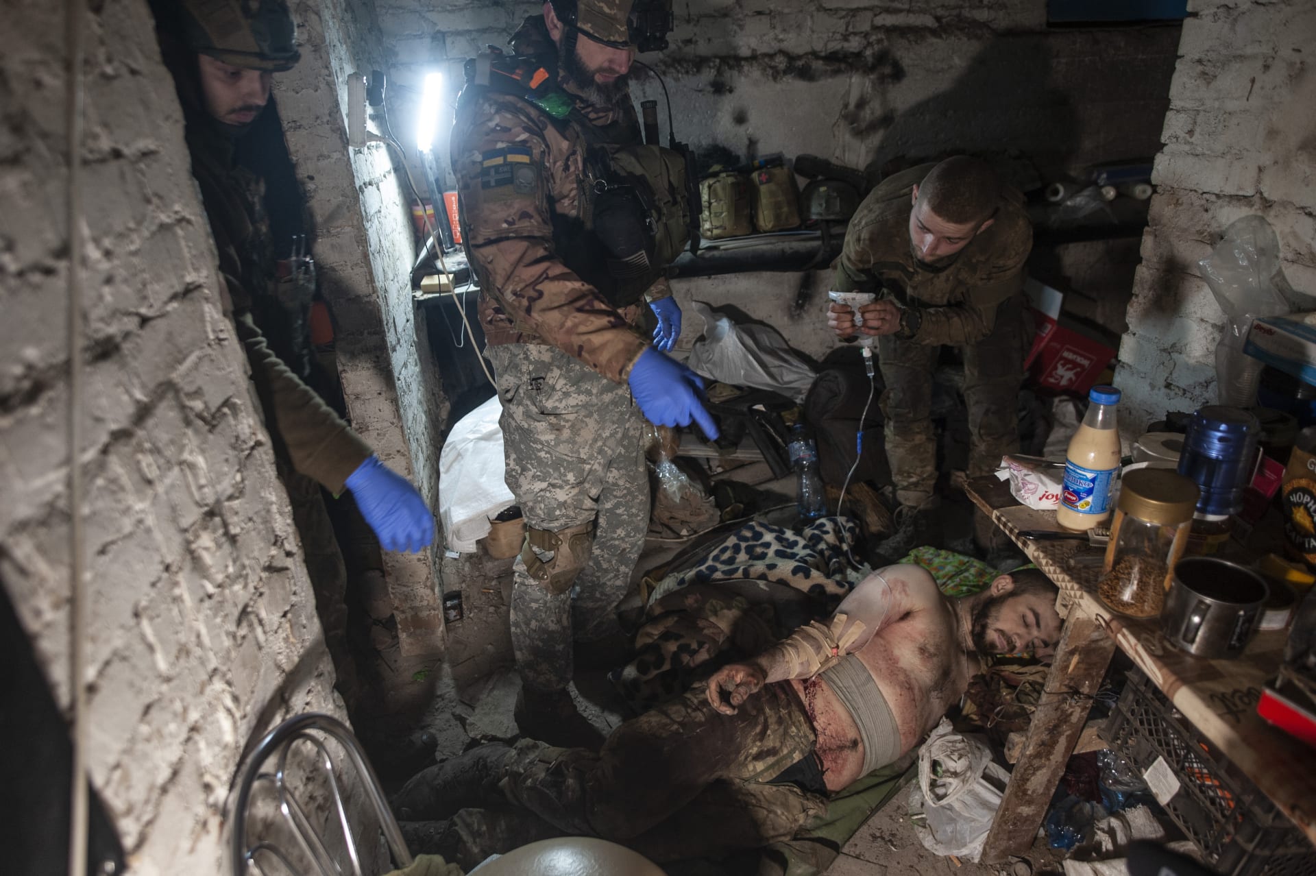 Ukrajinští vojáci poskytují první pomoc svému zraněnému spolubojovníkovi v krytu v Bachmutu