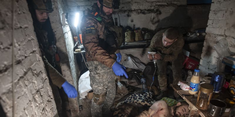 Ukrajinští vojáci poskytují první pomoc svému zraněnému spolubojovníkovi v krytu v Bachmutu