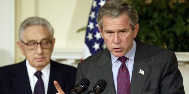 George Bush mladší vyhlašuje po útocích z 11. září protiteroristické zákony, Kissinger stojí v pozadí.