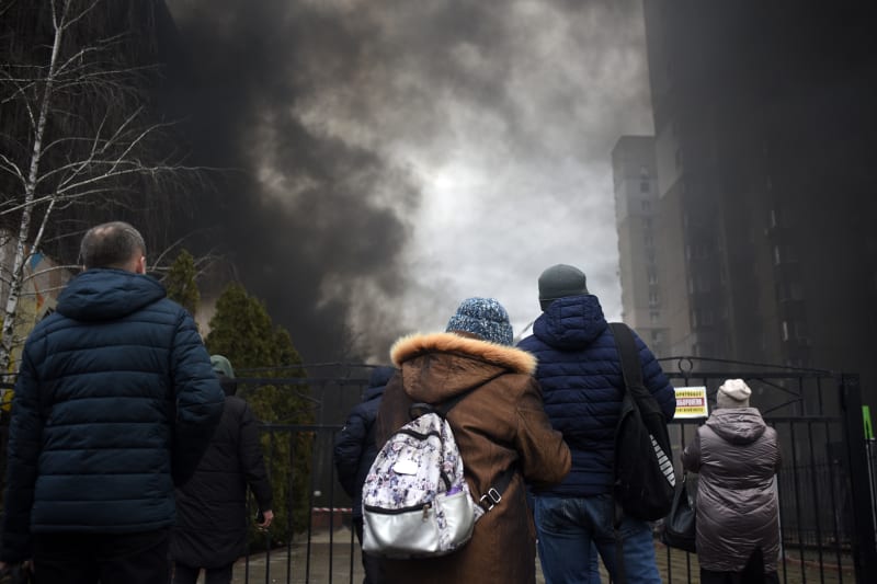 Místní sledují kouř stoupající z požáru, který způsobily trosky raket dopadajících na dvůr obytného domu v Kyjevě. (9.3.2023)