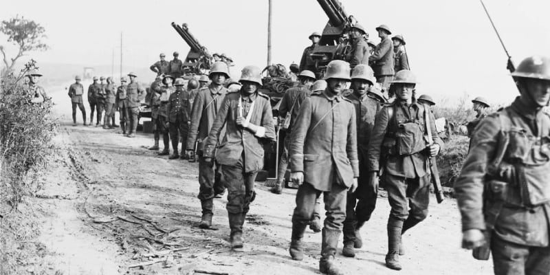 Zajatí němečtí vojáci procházejí kolem protiletadlových děl