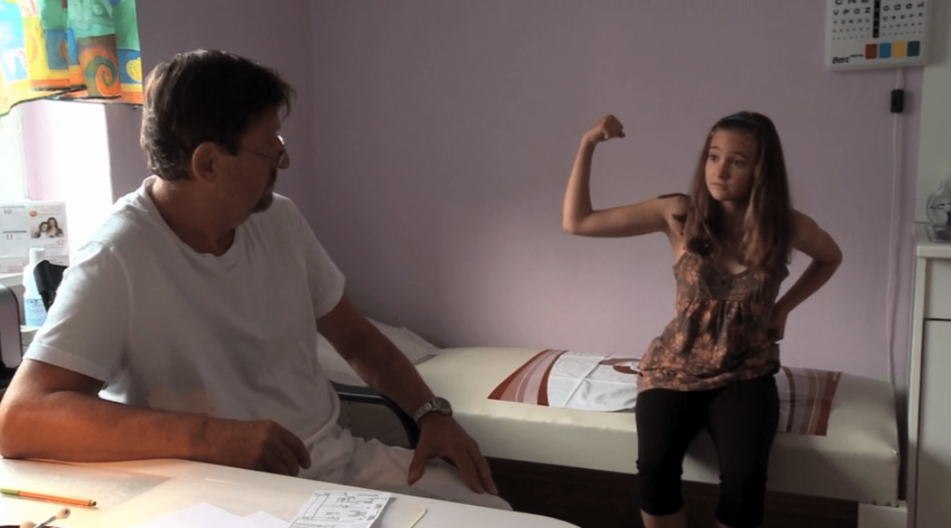 Starší dcera Karolína ukazuje lékaři, jaké má svaly na rukou z toho, jak u rodičů nosí krabice