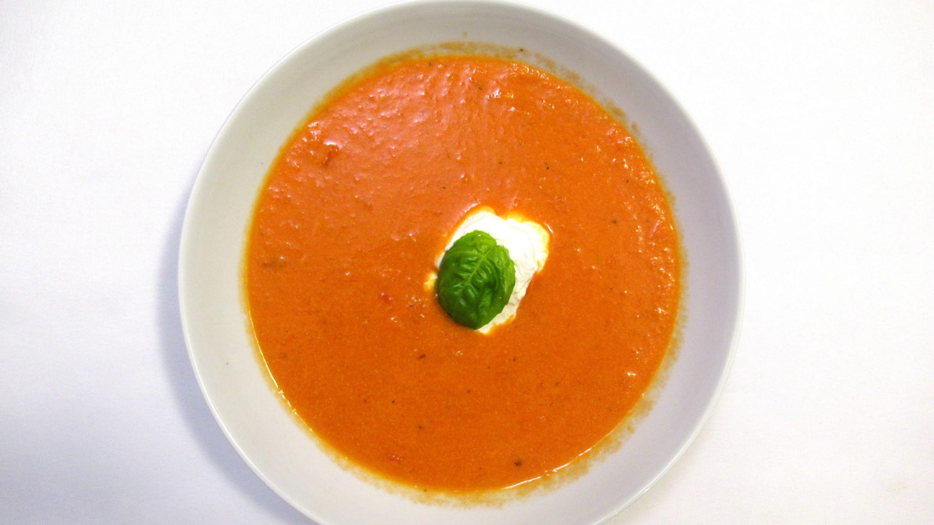 Rajčatová polévka sypaná parmezánem, zakápnutá smetanou, čerstvá bazalka