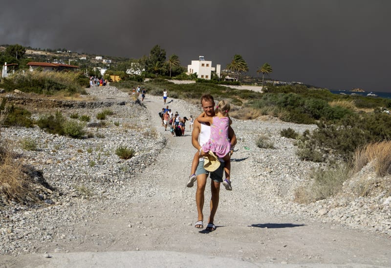Muž s dítětem v náručí prchá před požárem na Rhodu.