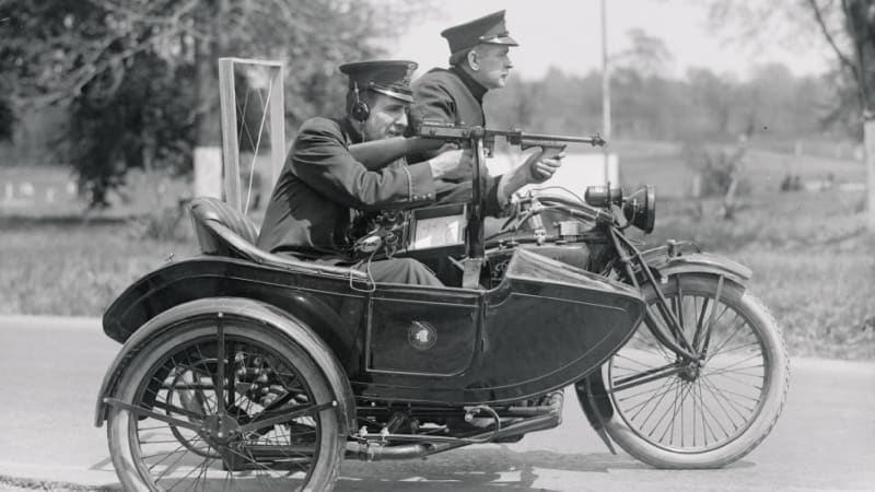 Dva policisté na motocyklu předvádějí samopal Thompson a bezdrátovou vysílačku umožňující spojení s policejní stanicí (1921)