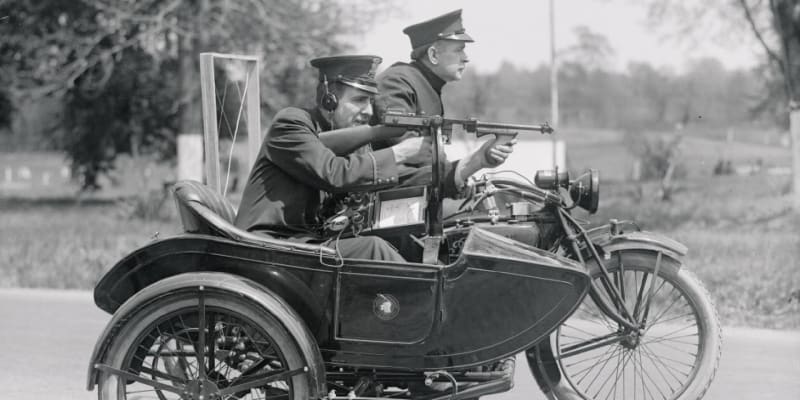 Dva policisté na motocyklu předvádějí samopal Thompson a bezdrátovou vysílačku umožňující spojení s policejní stanicí (1921)