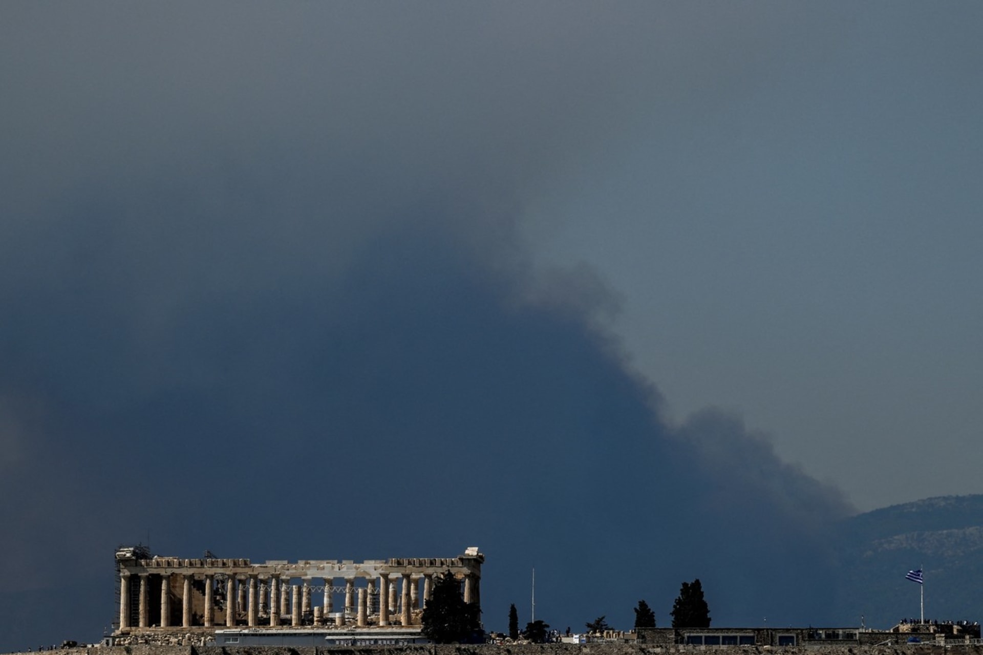 Dým se valí za starověkým chrámem Parthenon na vrcholu kopce Akropole, když na předměstí Atén 22. srpna 2023 zuří lesní požár. 