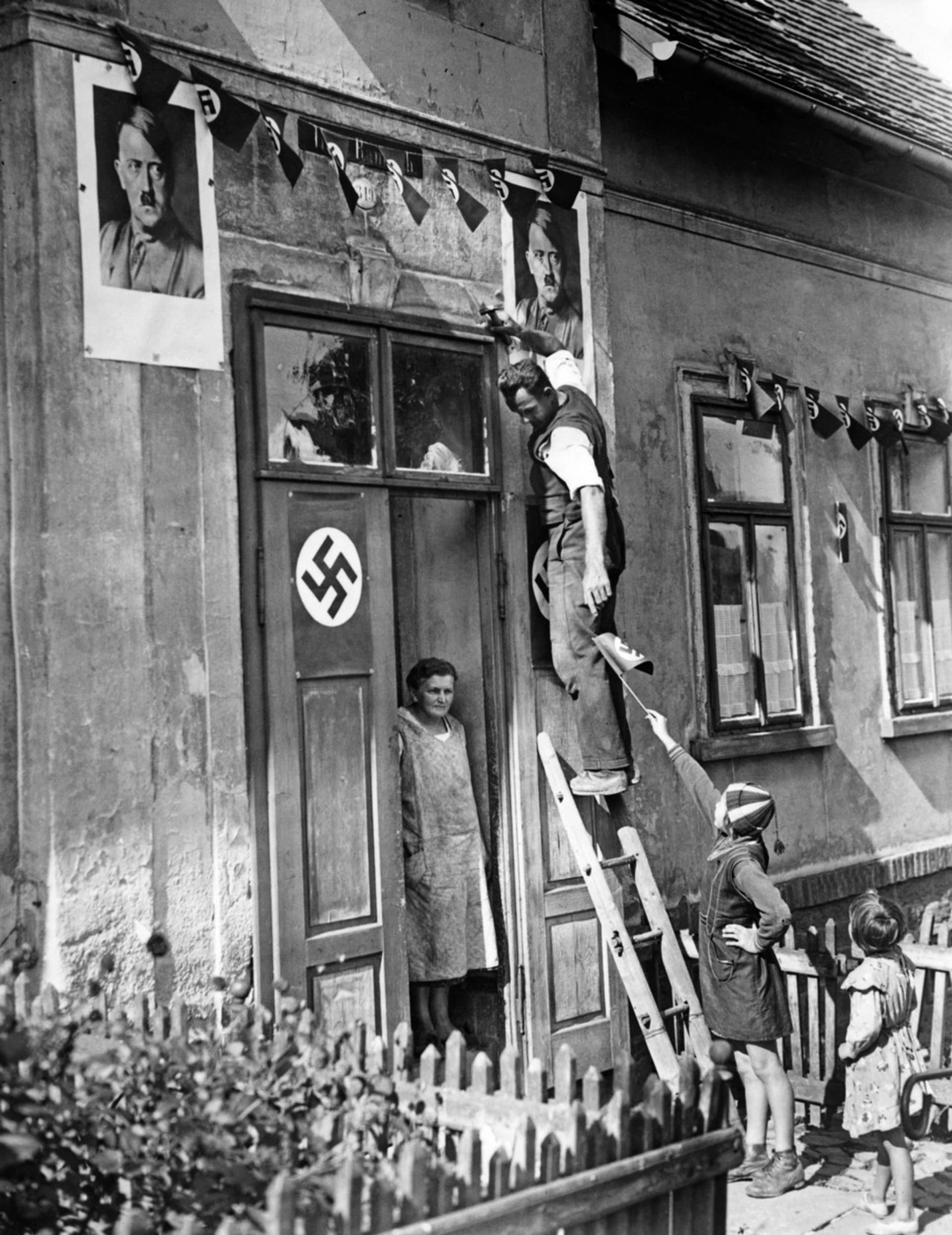 Obyvatelé Rumburku zkrášlují své domy nacistickými symboly (září 1938)