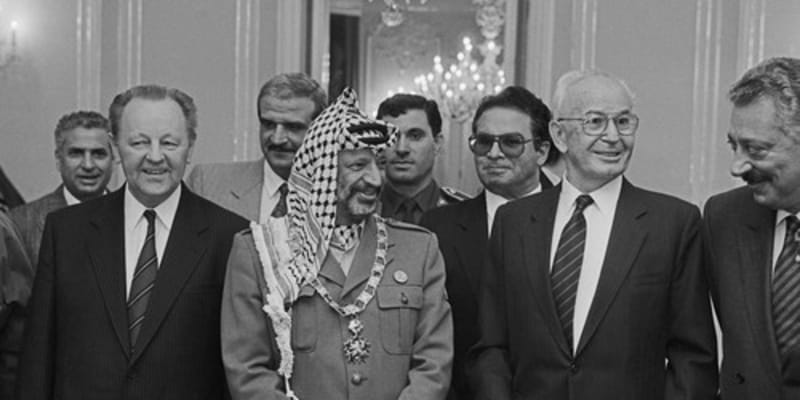 Návštěva Jásira Arafata v Praze, 18. října 1989. Do Československa tehdy přijel i Bassam Abu Sharif (s brýlemi za Husákem), podle amerického časopisu Time nejznámější tvář palestinského teroru. Prezident ČSSR Gustáv Husák předal na Pražském hradě předsedovi výkonného výboru OOP Jásiru Arafatovi Československý řád Bílého lva I. třídy.