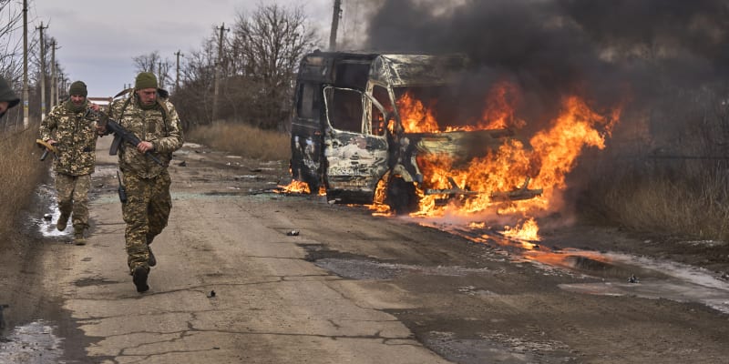 Ukrajinští vojáci míjí hořící vozidlo.
