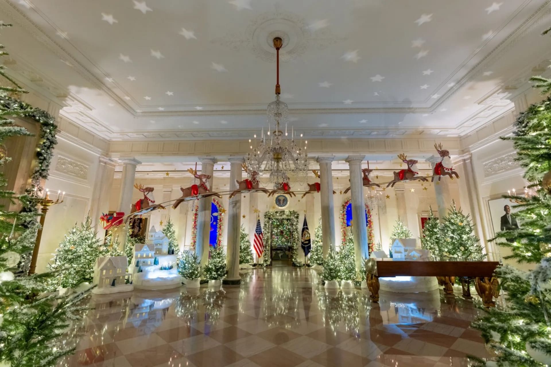 Vánoční výzdoba Bílého domu 2023: Santa Claus na saních a spřežení sobů prolétávají sloupy vstupní haly Bílého domu.