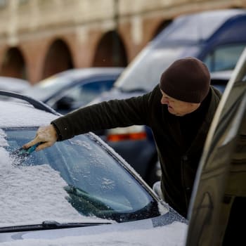 Muž v Praze oškrabává námrazu z auta