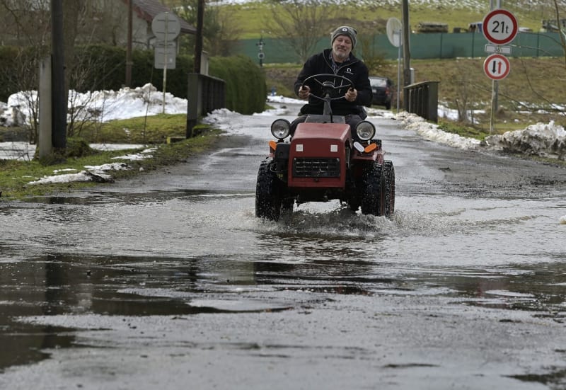Muž jede na zahradním traktoru po silnici zaplavené rozvodněnou říčkou Balinka.