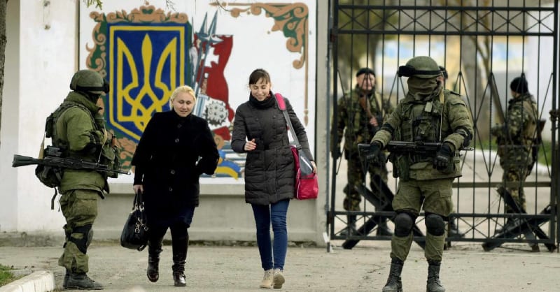 Příbuzné ukrajinských vojáků ze základny v krymském Simferopolu míjejí neoznačené ruské ozbrojence (19. března 2014)