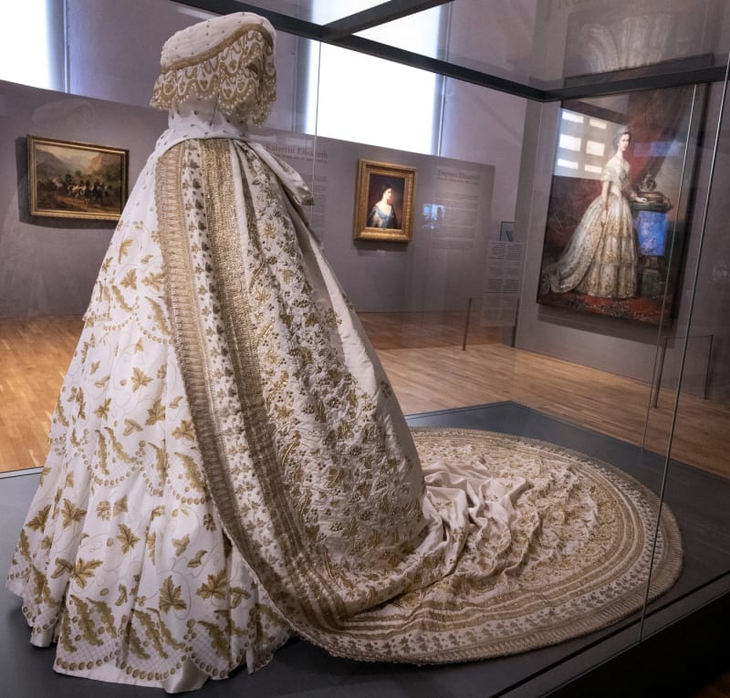 Replika pravděpodobných svatebních šatů císařovny Sissi s tajemným portrétem v pozadí