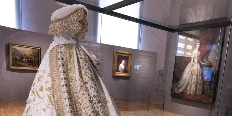 Replika pravděpodobných svatebních šatů císařovny Sissi s tajemným portrétem v pozadí